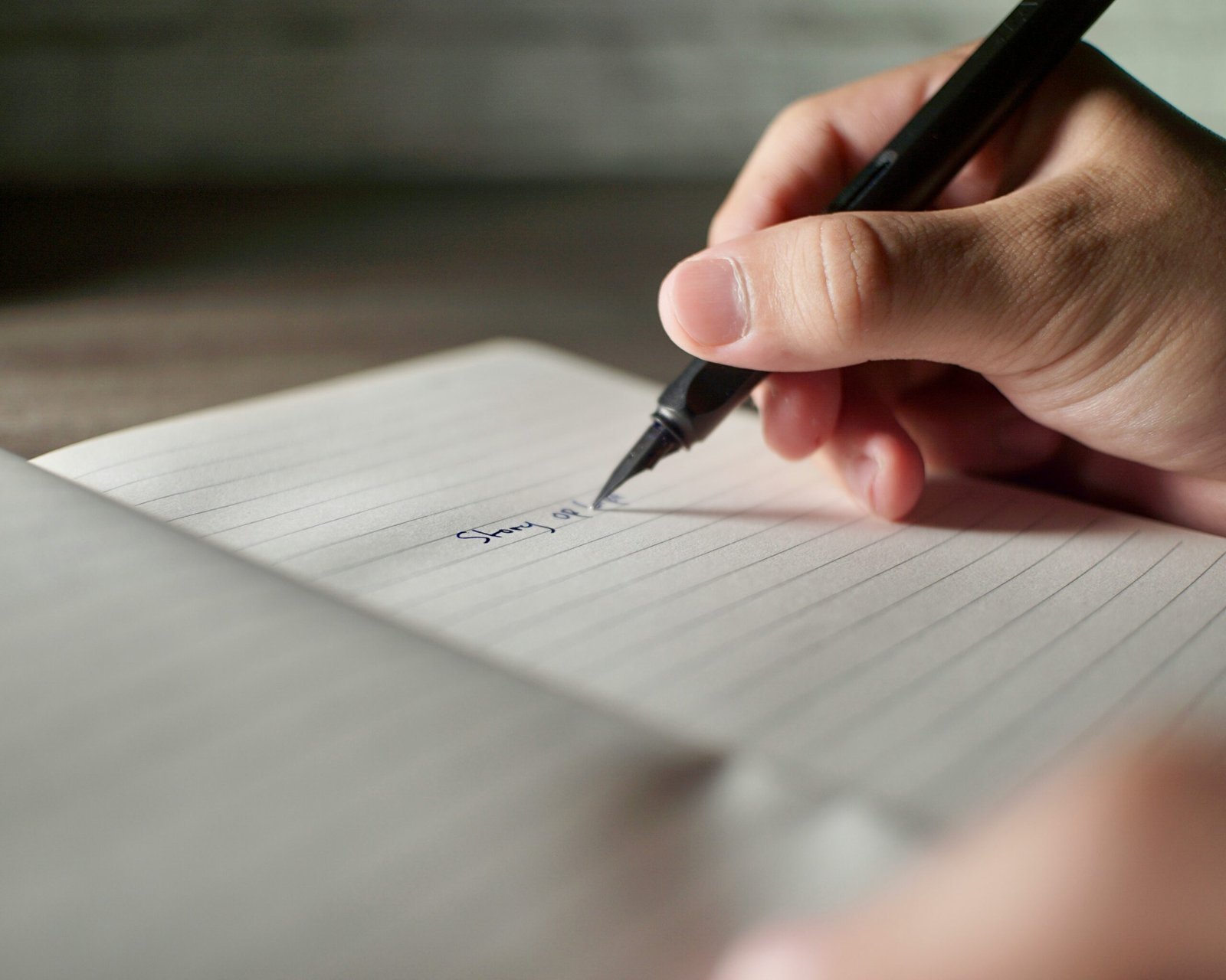 Close up of hands writing notes with a black ink pen on paper journal