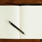 Two physical notebooks open on a wooden table with a pen for analog task management